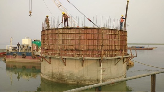 Large cylindrical water tank construction over water with workers and equipment